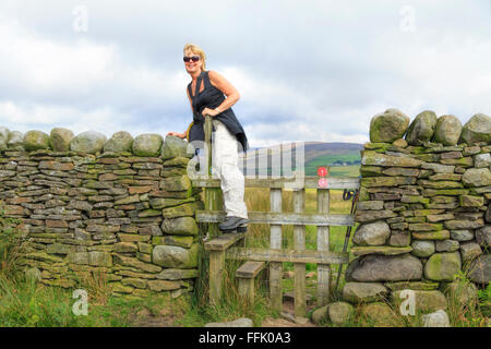 Female hiker grimpant sur un stile, Nicky Nook, creux de Bowland, Lancashire, Angleterre, Royaume-Uni. Banque D'Images