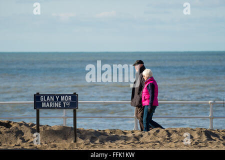 Aberystwyth, Pays de Galles, Royaume-Uni. 15 février 2016. Météo France : un couple de profiter d'une journée d'hiver au chaud soleil de marcher le long de la promenade à Aberystwyth, qui est encore partiellement recouverte de sable et de galets lavés par la tempête féroce Imogen il y a exactement une semaine. De nombreuses écoles ont pris leurs vacances cette semaine. Credit : Keith morris/Alamy Live News Banque D'Images