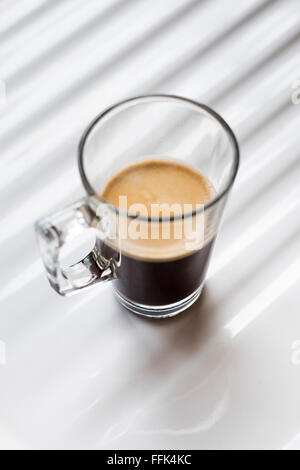 Café noir dans une tasse en verre clair sur fond blanc Banque D'Images