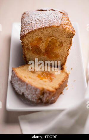 Un pain gâteau kumquat surmonté de sucre glace, une tranche, sur une assiette blanche Banque D'Images