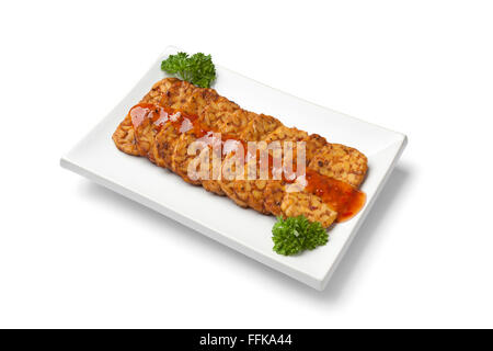 Tranches de tempeh frit avec sauce chili sur un plat sur fond blanc Banque D'Images