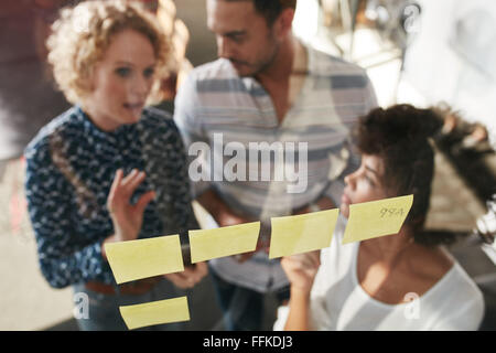 Trois personnes ayant une réunion de bureau. Ils sont debout en face de paroi en verre avec post it et de discussions. Banque D'Images