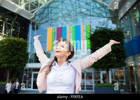 Smiling businesswoman with hands up contre bâtiment moderne Banque D'Images