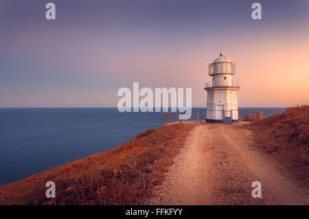 Beau vieux phare blanc sur le littoral de l'océan sur la montagne, au coucher du soleil. Summer seascape Banque D'Images