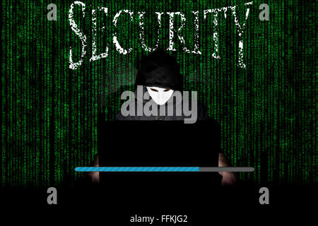 Un homme masqué à un ordinateur portable symbolisant les dangers de l'Internet. Banque D'Images