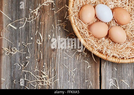 Vue de dessus du nid de pâques avec des oeufs incolores avec de la paille sur une table en bois Banque D'Images