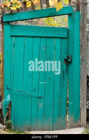 Vieille porte en bois dans le jardin. Un portail peint vert n'est plus droite, et est verrouillé avec un cadenas. Banque D'Images