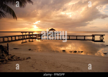 Lever du soleil sur la côte du Belize. Une jetée avec un toit de chaume est silhouetté contre le ciel. Banque D'Images