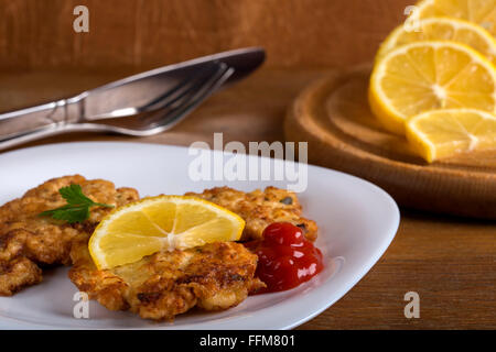 Le ketchup avec un Wiener Schnitzel et de tranches de citron sur plaque blanche avec fond de bois Banque D'Images