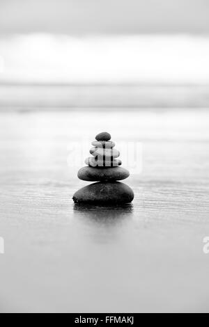 L'équilibrage de cailloux sur une plage de tempête dans la lumière du matin. Noir et blanc. Selective focus Banque D'Images