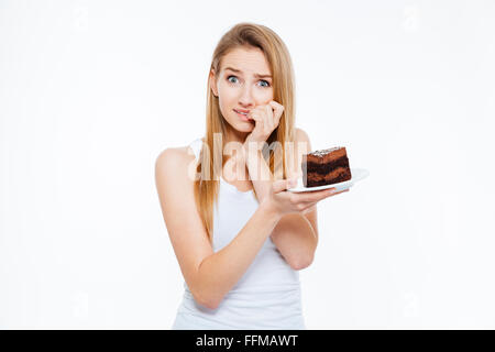 Jolie jeune femme douteuse la réflexion sur l'alimentation et la tenue du gâteau sur fond blanc Banque D'Images