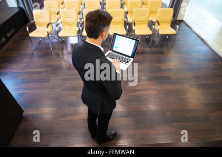 Vue arrière de man et à l'aide d'ordinateur portable en salle de conférence Banque D'Images