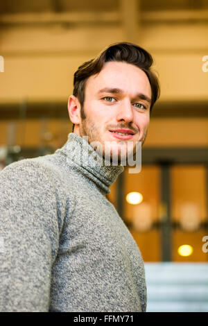 Taille Young Man Wearing Sweater Standing with Hand on Chin à la recherche de l'école dans le couloir réfléchie wit Banque D'Images