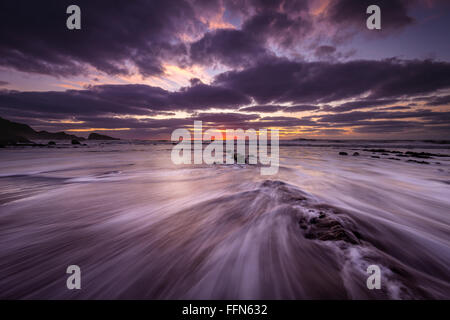 Débit d'ondes sur le sable et rochers au coucher du soleil à Welcombe Bouche Beach dans le Nord du Devon, Royaume-Uni. Banque D'Images