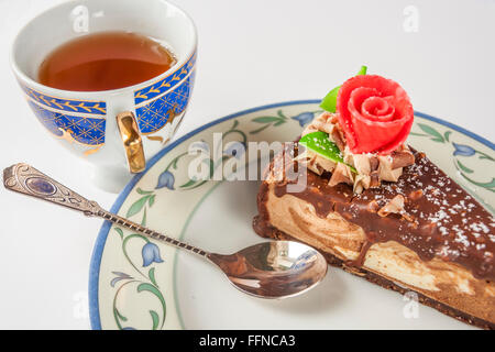 Tranche de gâteau au chocolat à la main sur une soucoupe avec cuillère et tasse de thé noir Banque D'Images