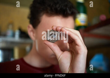 Teenage boy holding un écrou de vis rouillées et regardant à travers elle Banque D'Images