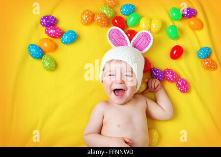 Baby Boy in bunny hat lying on couverture jaune avec des oeufs de pâques Banque D'Images