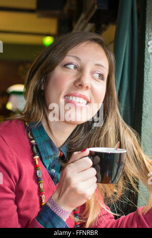 Jeune brunette habillée en rouge de boire du café au café Banque D'Images