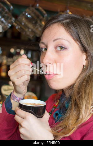 Jeune brunette habillée en rouge à boire du café avec une cuillère Banque D'Images