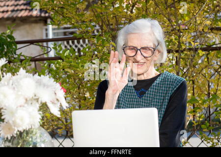 Femme de 90 ans tout en ayant un signe un appel vidéo sur un ordinateur portable blanc Banque D'Images