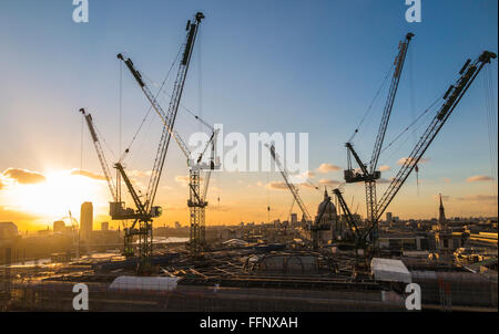 Grues à tour sur le nouveau site de développement office Bloomberg Place dans la ville de London, EC4 qui se découpent sur l'horizon sur fond de ciel bleu au coucher du soleil Banque D'Images