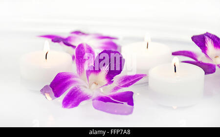 Les fleurs d'orchidées tropicales et blanc allumé des bougies flottant dans l'eau. Banque D'Images