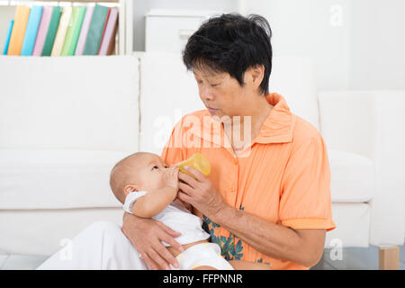 Nounou en prenant soin de bébé à la maison. Se nourrir de la nourriture solide la purée de fruits avec une bouteille. Banque D'Images