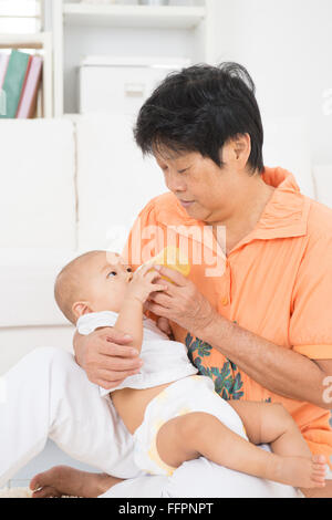 Grand-mère en prenant soin des petits-enfants à la maison. Se nourrir de la nourriture solide la purée de fruits avec une bouteille. Banque D'Images