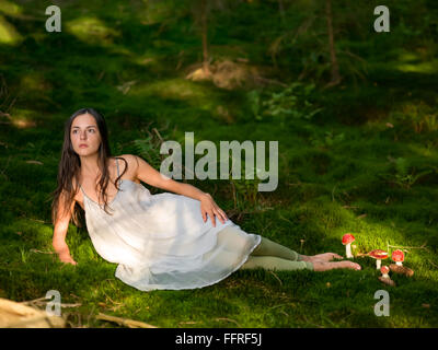 Belle femme dans la forêt habillé comme une fée se trouve sur vert mousse avec l'amanite toxique à la Banque D'Images