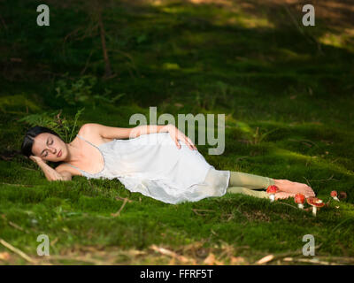 Belle femme dans la forêt habillé comme une fée se trouve sur vert mousse avec le couchage Amanita toxiques Banque D'Images