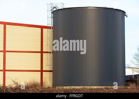 Grand bâtiment de stockage silo ou noir avec une échelle en aluminium ou en acier à l'extérieur. Bâtiment jaune et rouge derrière l'échelle. Banque D'Images