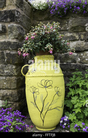 Décoration ancienne urne avec planté des fleurs dans un jardin contre mur de pierre. Banque D'Images