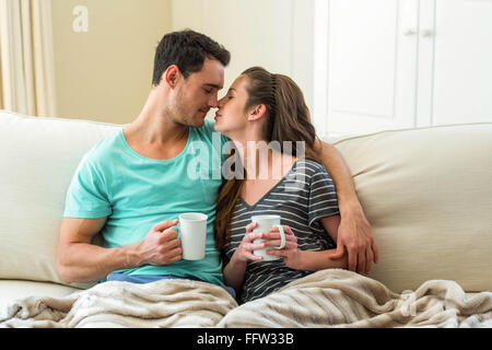 Jeune couple de câlins sur canapé tandis que le café Banque D'Images