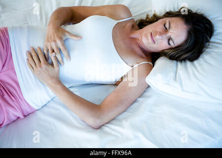 Tired woman Lying in Bed serrant son estomac Banque D'Images