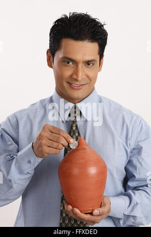 Businessman holding petit pot en terre d'économie d'une main et mettre dans la fente 1 roupie coin à l'intérieur M.# 703T Banque D'Images