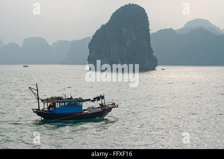 Un petit bateau de pêche motoring dans une mer calme dans la baie d'Halong avec Misty karsts calcaire derrière le Vietnam Banque D'Images