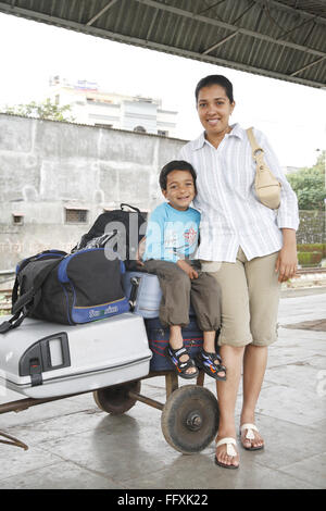 Mère et fils debout assis sur les bagages enregistrés conservés sur chariot MR# 468 Banque D'Images