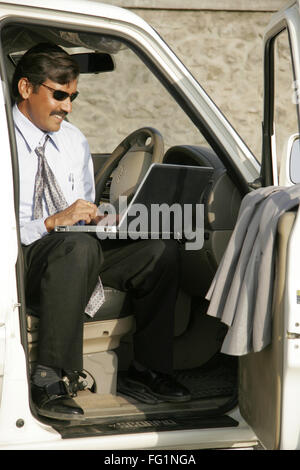 Homme d'affaires indien en manteau gris portant des lunettes noires sitting in car and using laptop M.# 686B Banque D'Images