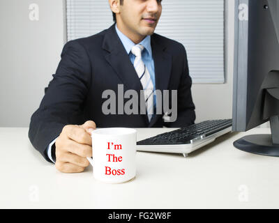 Exécutif multitâche holding mug looking at computer M.# 779K Banque D'Images