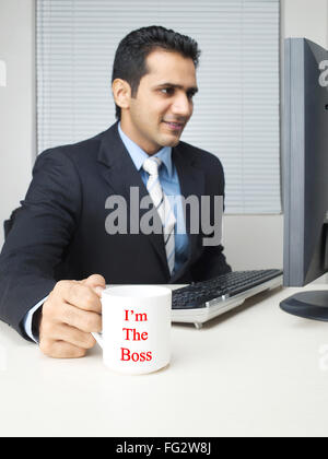Exécutif multitâche holding mug looking at computer M.# 779K Banque D'Images