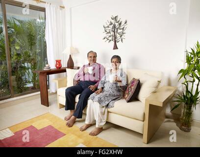 Vieux couple montrant tasses blanc sitting on sofa MR# 702T, 702S Banque D'Images