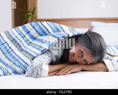 Vieille dame couchée sur le lit en tenant pour couvrir elle-même M.# 702S Banque D'Images