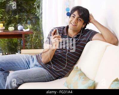 Young man listening to music on headphones sitting on sofa MR# 702V Banque D'Images