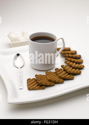 Tasse de thé noir en plat de service avec des morceaux de sucre et de biscuits en Inde Banque D'Images