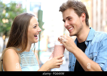 Couple ou entre amis le partage d'un milkshake et rire dans la rue Banque D'Images