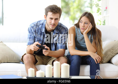 L'homme jouant des jeux vidéo à la maison et sa petite amie s'ennuyer à côté de le regarder Banque D'Images