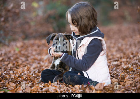 Chiot Boxer assis avec petite fille dans les feuilles d'automne Banque D'Images