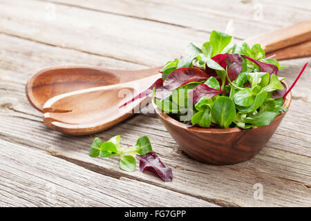 Feuilles de salade de maïs dans un bol et les ustensiles sur la table en bois. Valerianella locusta Banque D'Images