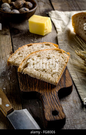 Pain au levain, morceau de fromage, œufs de caille, les épis de blé d'or et le couteau sur la table en bois rustique. La nourriture rustique still life Banque D'Images