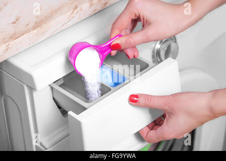 Femme jette de lessive dans une machine à laver. Banque D'Images